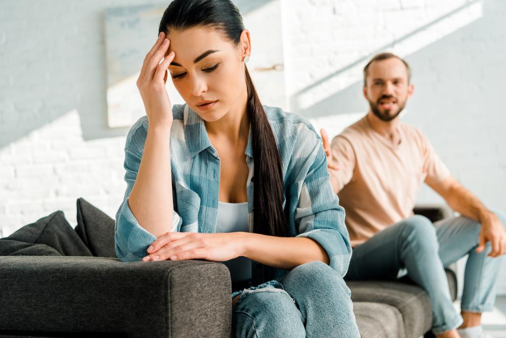 stressed wife with hand on head sitting on foreground after arguing with husband at home - Photo, Image