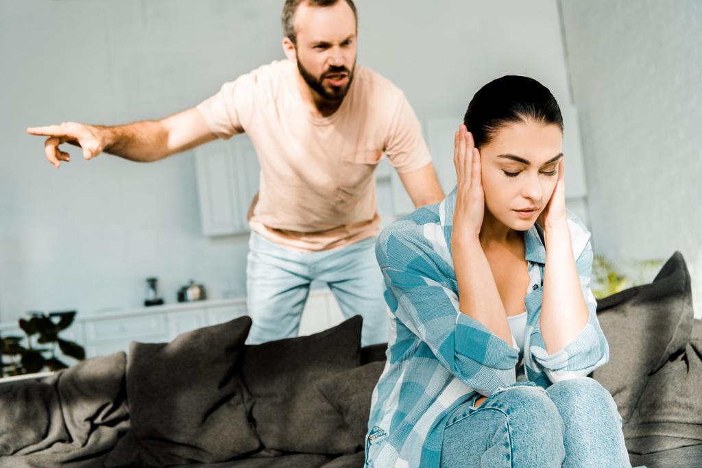 angry husband shouting at wife sitting on sofa and covering ears with hands - Photo, Image