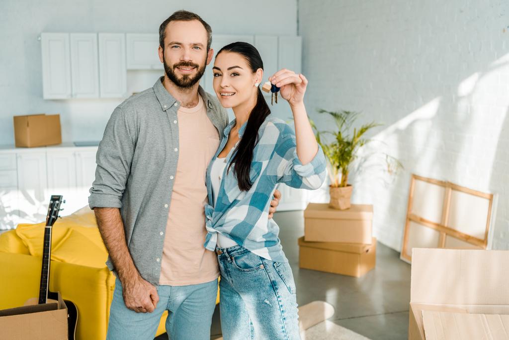 smiling couple looking at camera and wife holding keys from new house, moving concept - Photo, Image