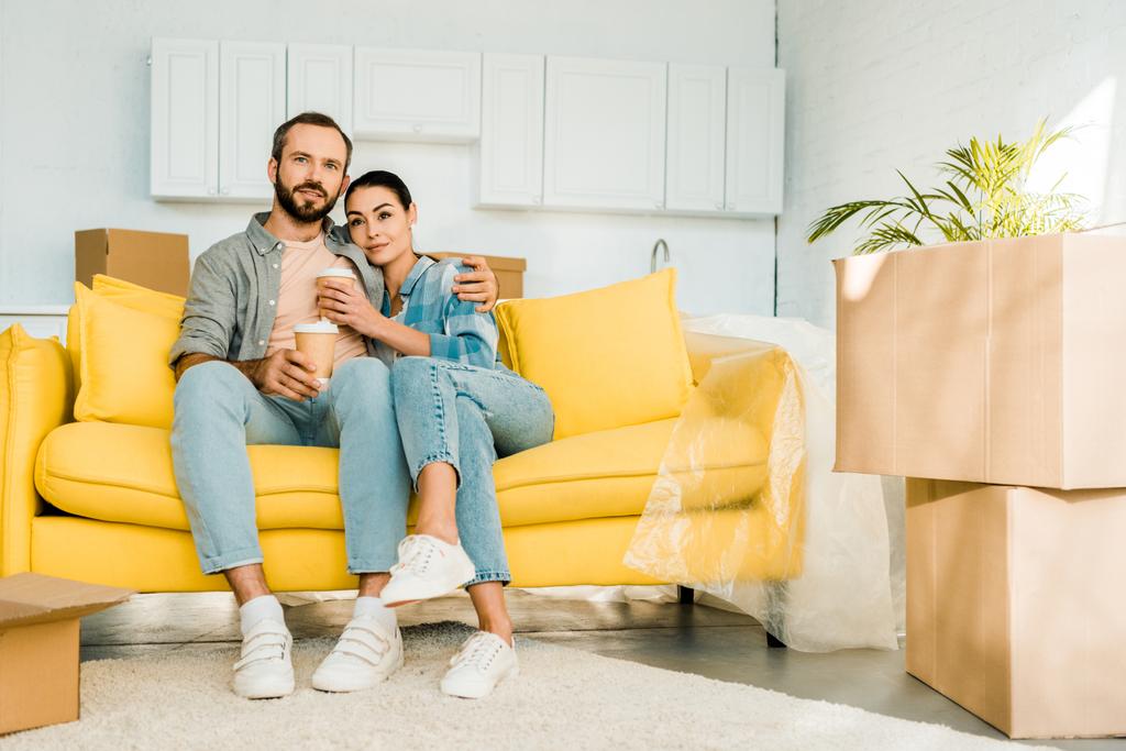 aviomies ja vaimo istuvat sohvalla ja juovat kahvia pakatessaan uuteen taloon, liikkuva käsite
 - Valokuva, kuva
