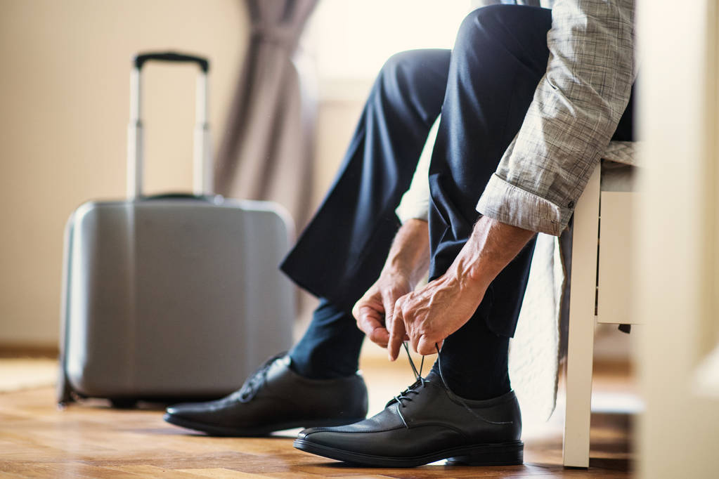 Midsection of businessman on a business trip sitting in a hotel room, tying shoelaces. - Photo, Image