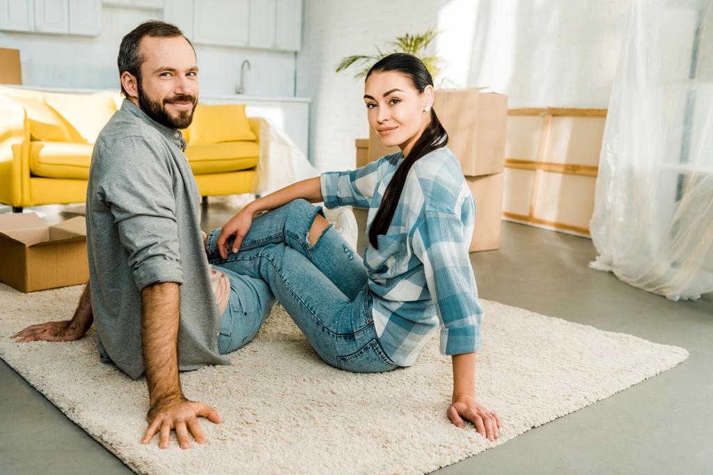 Glimlachende man en vrouw zittend op de vloer en rust na de verpakking voor nieuw huis, bewegende concept - Foto, afbeelding