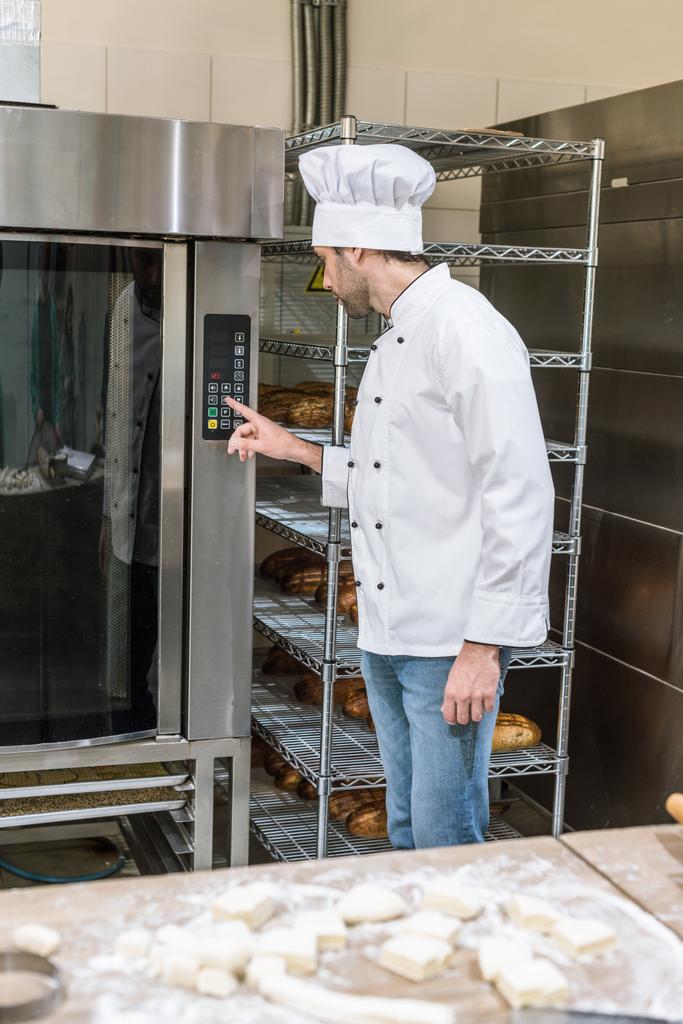 panadero masculino pulsar botón en el horno en la cocina
 - Foto, imagen