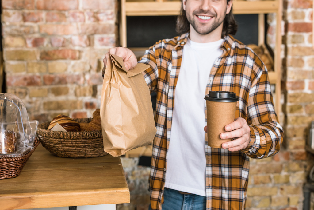 pastanede gitmek gülümseyen adam pasta ve kahve ile kağıt torba tutarak - Fotoğraf, Görsel