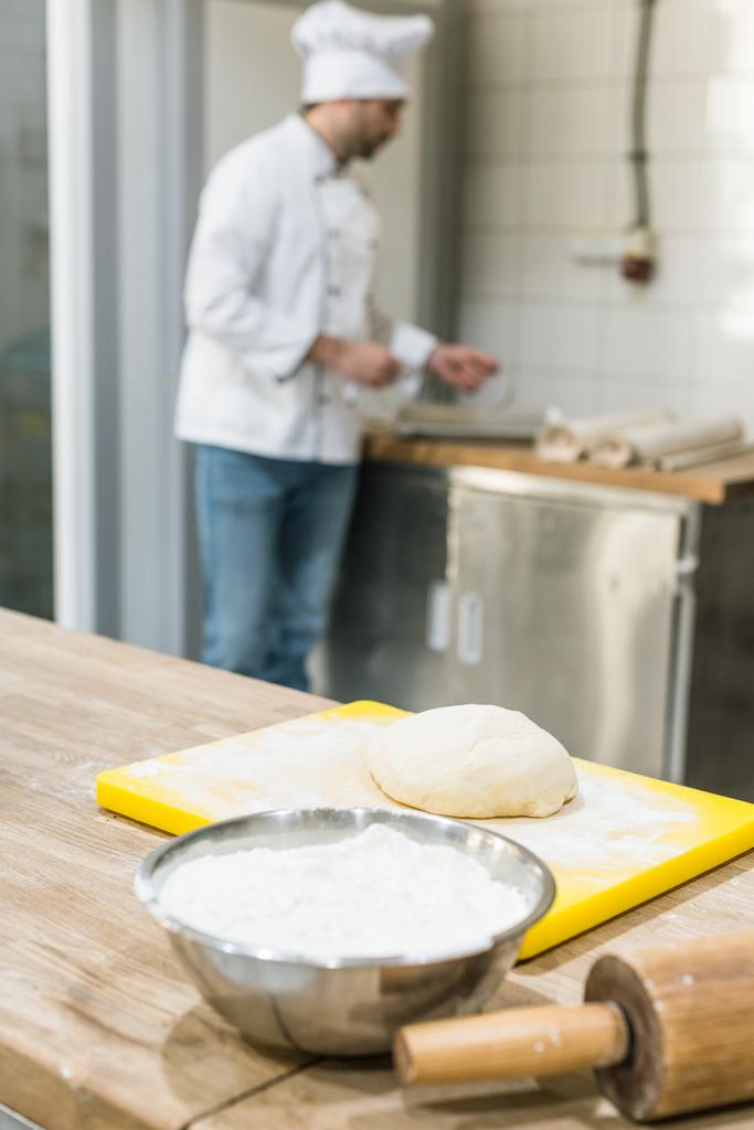 Erwachsener Bäcker in Koch-Uniform bereitet Teig an der Theke zu - Foto, Bild