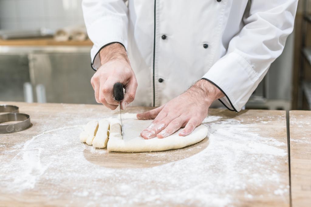 close up of baker hands cutting dough on wooden table - Photo, Image