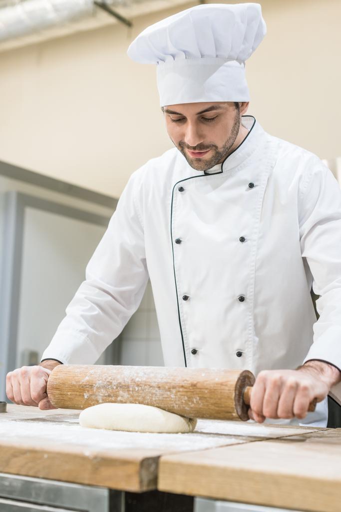 Schöner Bäcker rollt Teig auf Holztisch aus - Foto, Bild