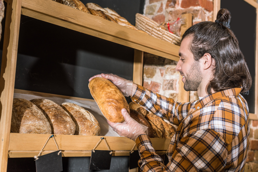 Zijaanzicht van verkoper nemen van vers gebakken brood in handen - Foto, afbeelding