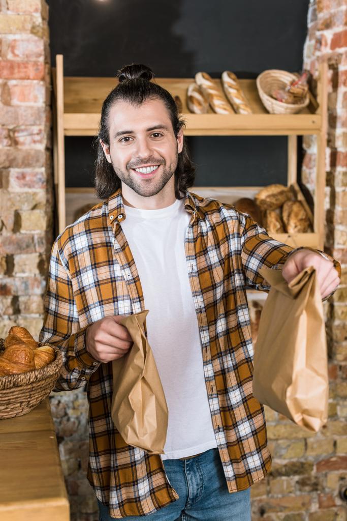 Smiling male seller holding paper bags in bakehouse - Photo, Image