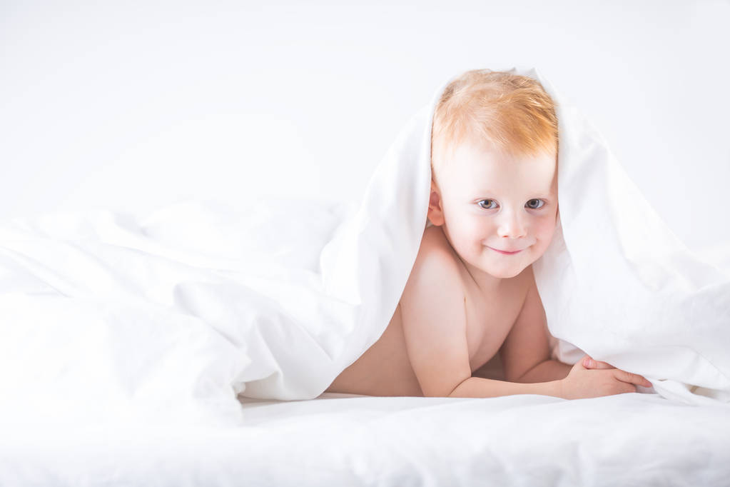Habby young smilling child boy in white bed. - Photo, Image