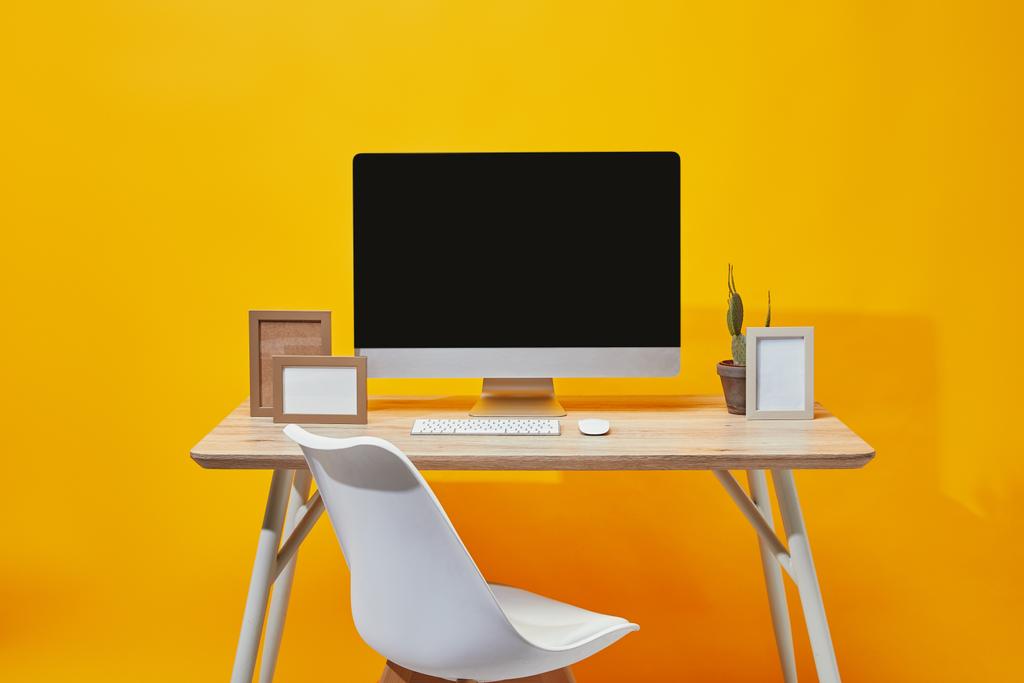 Computer, lege fotolijsten en cactus in bloempot aan houten tafel op geel  - Foto, afbeelding