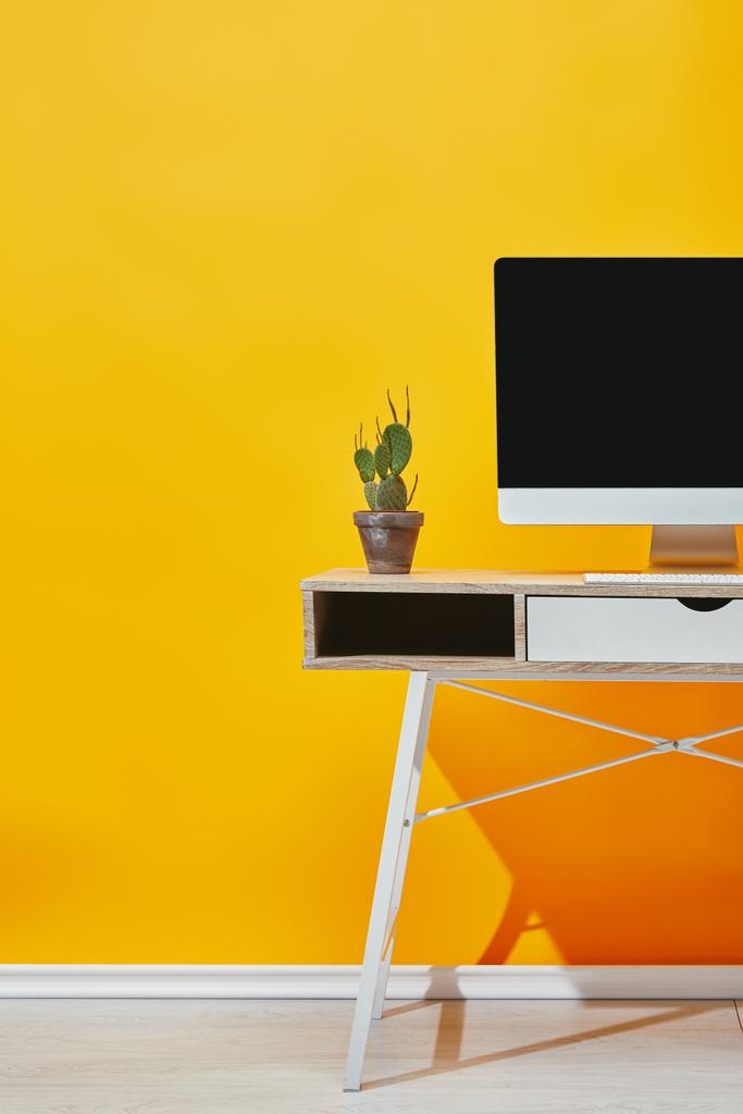 Cactus en maceta y ordenador en mesa de madera cerca de la pared amarilla
 - Foto, imagen