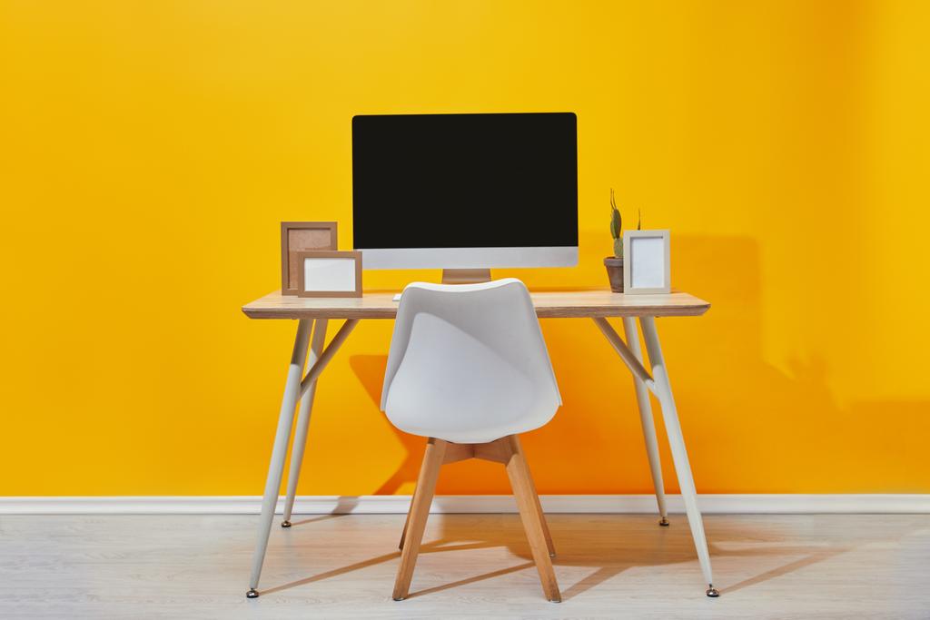 Υπολογιστή, ψηφιακές κορνίζες φωτογραφιών και κάκτος στον εργασιακό χώρο κοντά σε κίτρινο τοίχο - Φωτογραφία, εικόνα