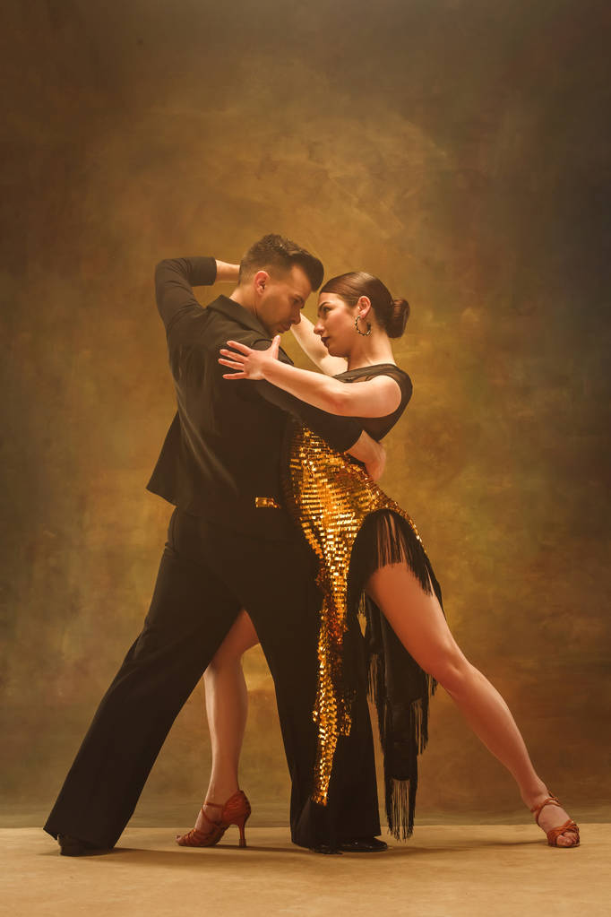 Tańca towarzyskiego para w złota sukienka taniec na tle studio. - Zdjęcie, obraz