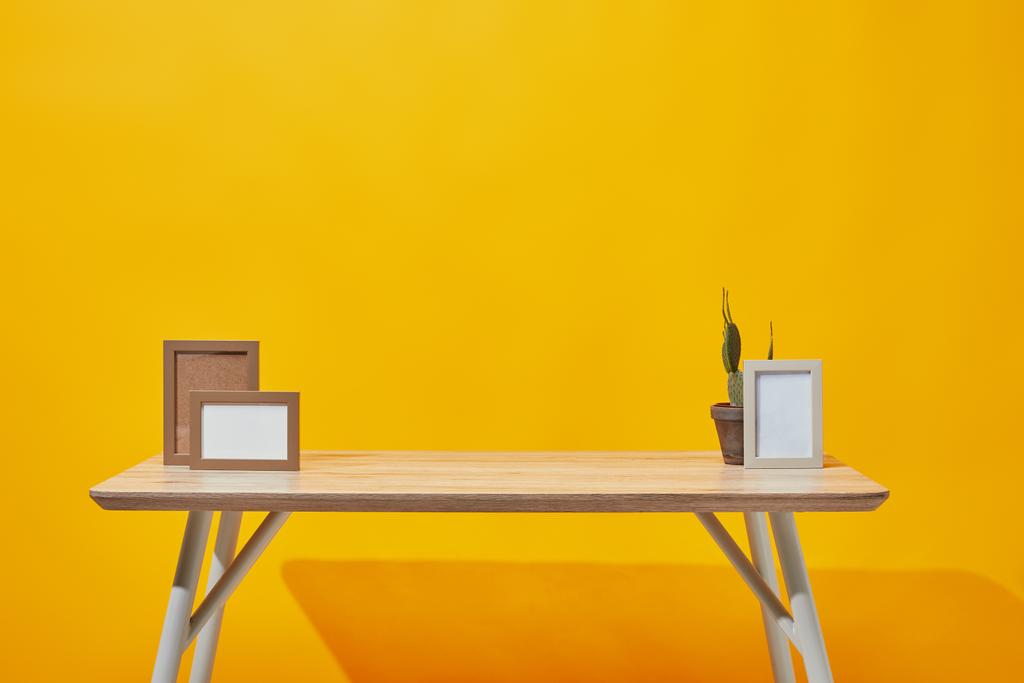 Mesa de madera con marcos de fotos vacíos y cactus en maceta en amarillo
 - Foto, imagen