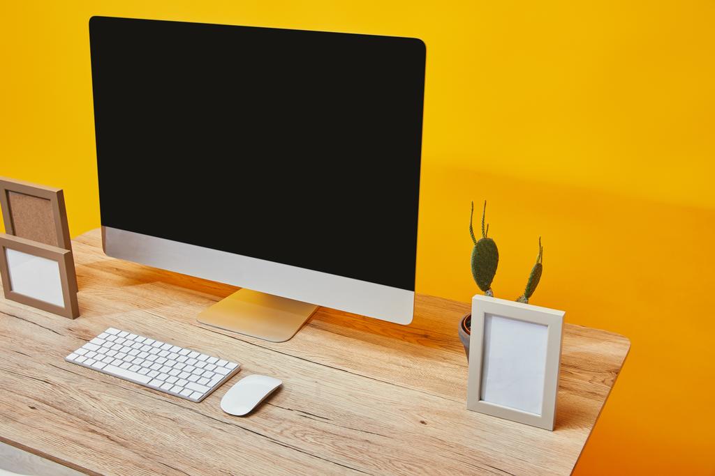 コンピューター、フォト フレームと黄色の壁の背景に木製のテーブルの上にサボテン - 写真・画像