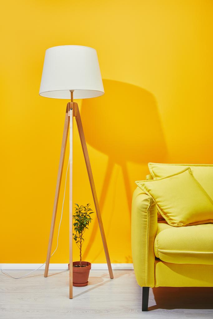 Sofa, Zimmerpflanze und Lampe in der Nähe der gelben Wand - Foto, Bild