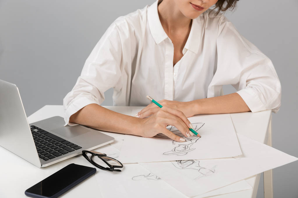灰色の壁背景描画テーブルに座って上分離された若いビジネス女性デザイナーのトリミング写真. - 写真・画像
