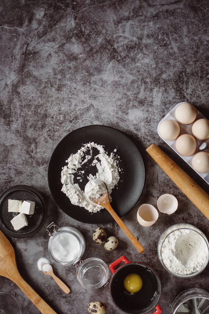 Ingrédients et ustensiles de cuisson. Déposer la farine, la vaisselle, les œufs, le sel de beurre et le rouleau à pâtisserie sur un fond gris. Pose plate. Espace texte
 - Photo, image