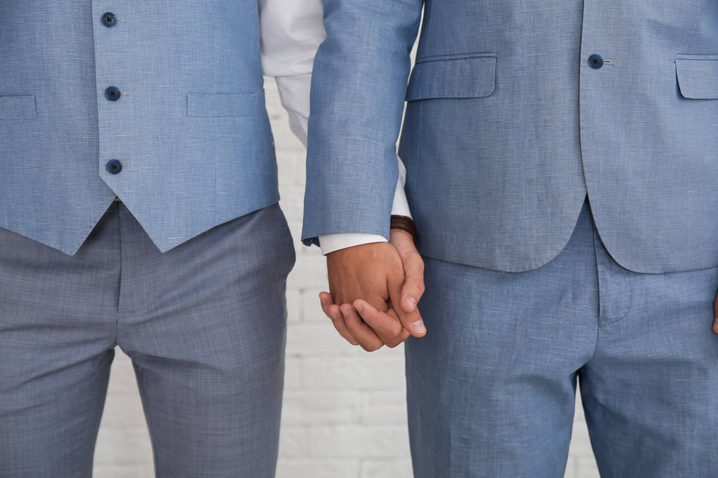 Νεόνυμφο γκέι ζευγάρι κρατώντας τα χέρια κοντά σε λευκό τοίχο, κοντινό πλάνο - Φωτογραφία, εικόνα