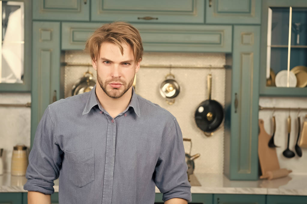 Homem com rosto sério em pé camisa azul na cozinha - Foto, Imagem