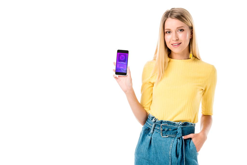 hermosa mujer joven sosteniendo teléfono inteligente con aplicación de compras en la pantalla y sonriendo a la cámara aislada en blanco
  - Foto, imagen