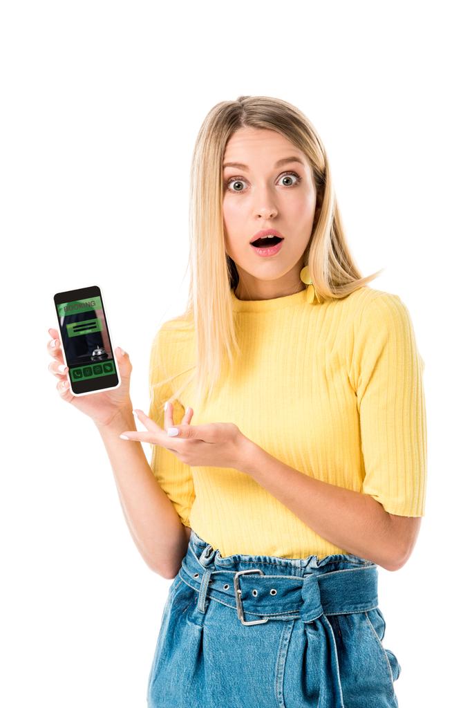 schockierte junge Frau hält Smartphone mit Buchungsanwendung auf dem Bildschirm und blickt in Kamera isoliert auf Weiß  - Foto, Bild