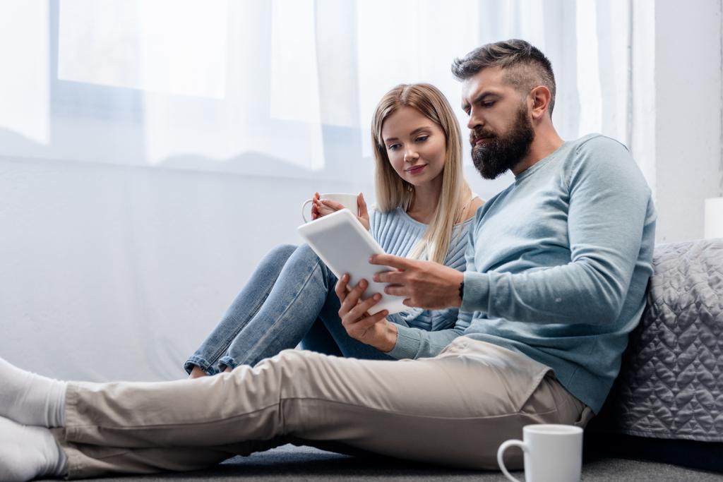 Couple sitting on floor with digital tablet and drinks - Photo, Image