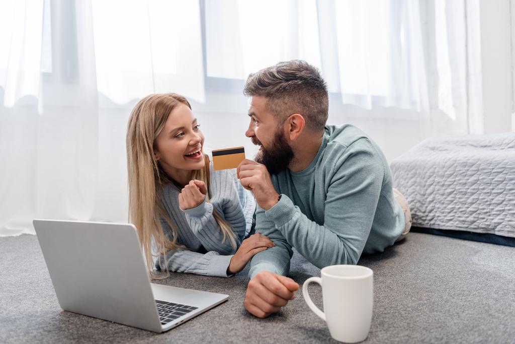 ノート パソコンとクレジット カードと床に横になっている笑顔のカップル - 写真・画像
