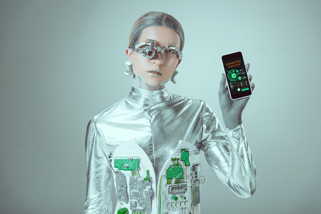 Robot trzyma smartphone z marketingu aplikacji analizy i patrząc na kamery na białym tle na koncepcji technologii przyszłości, szary    - Zdjęcie, obraz