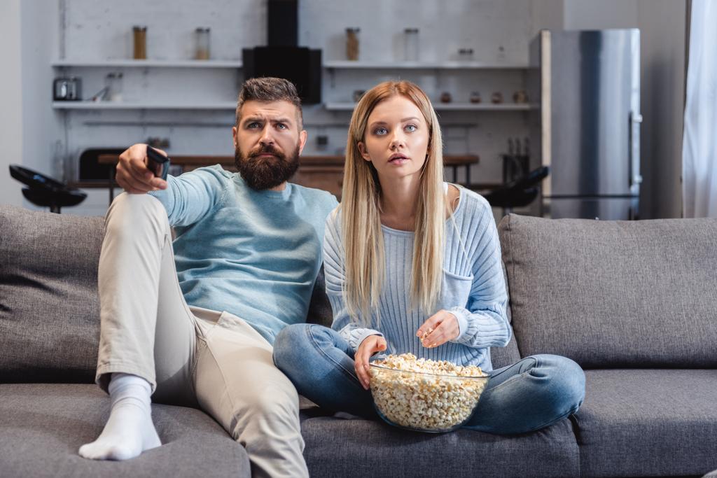 Sorpresa moglie seduta sul divano con marito e in possesso di popcorn
  - Foto, immagini