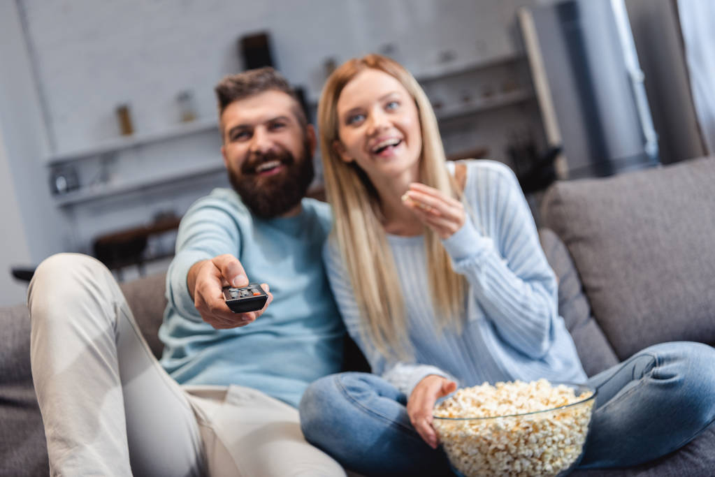 Happy couple sitting on sofa with popcorn and watching movie - Photo, Image