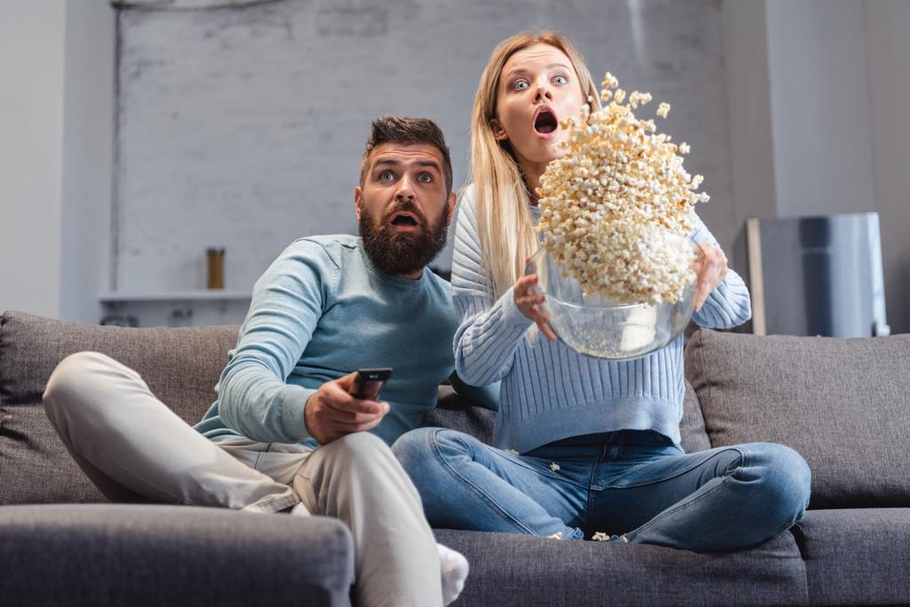 überraschte Frau verstreut Popcorn und sitzt mit Ehemann auf Sofa - Foto, Bild