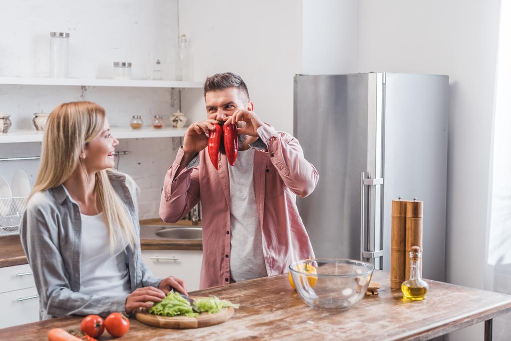 Веселый муж играет с овощами рядом с женой
 - Фото, изображение