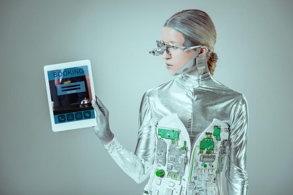 Серебряный робот глядя на планшет с устройством бронирования изолированы на сером, концепция технологии будущего
 - Фото, изображение