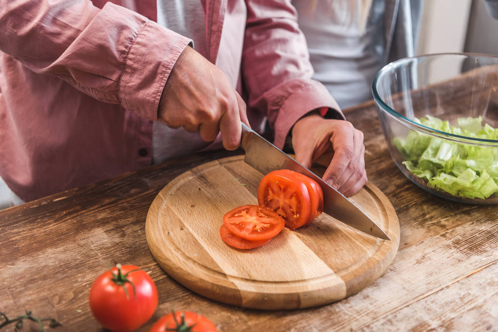 Vista recortada del hombre cortando tomate sobre tabla de madera en la cocina
  - Foto, imagen