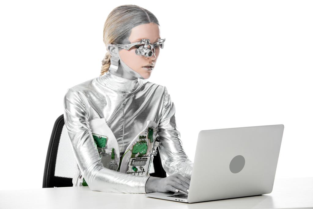 シルバー ロボットのテーブルに座って、白、将来技術概念に分離されたノート パソコンでの作業 - 写真・画像