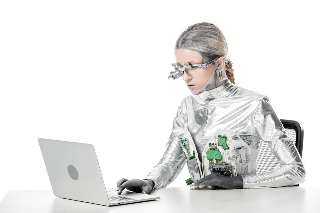 silver robot sitting at table and using laptop isolated on white, future technology concept - Photo, Image
