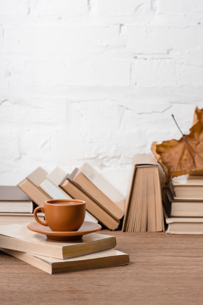 boeken, kopje koffie en droge Herfstblad op houten tafel - Foto, afbeelding