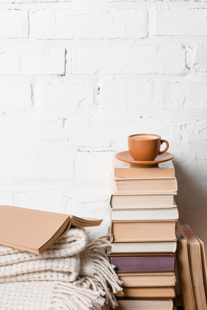 kopje koffie op stapel boeken in de buurt van witte bakstenen muur - Foto, afbeelding