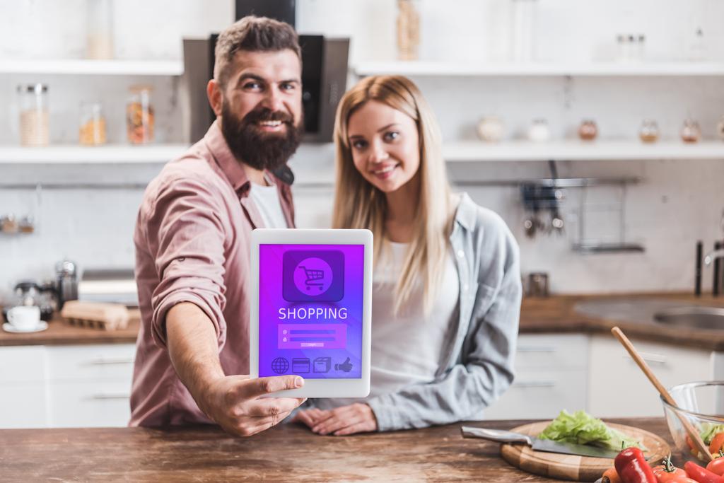 couple souriant tenant tablette numérique avec application de magasinage en ligne à l'écran
 - Photo, image