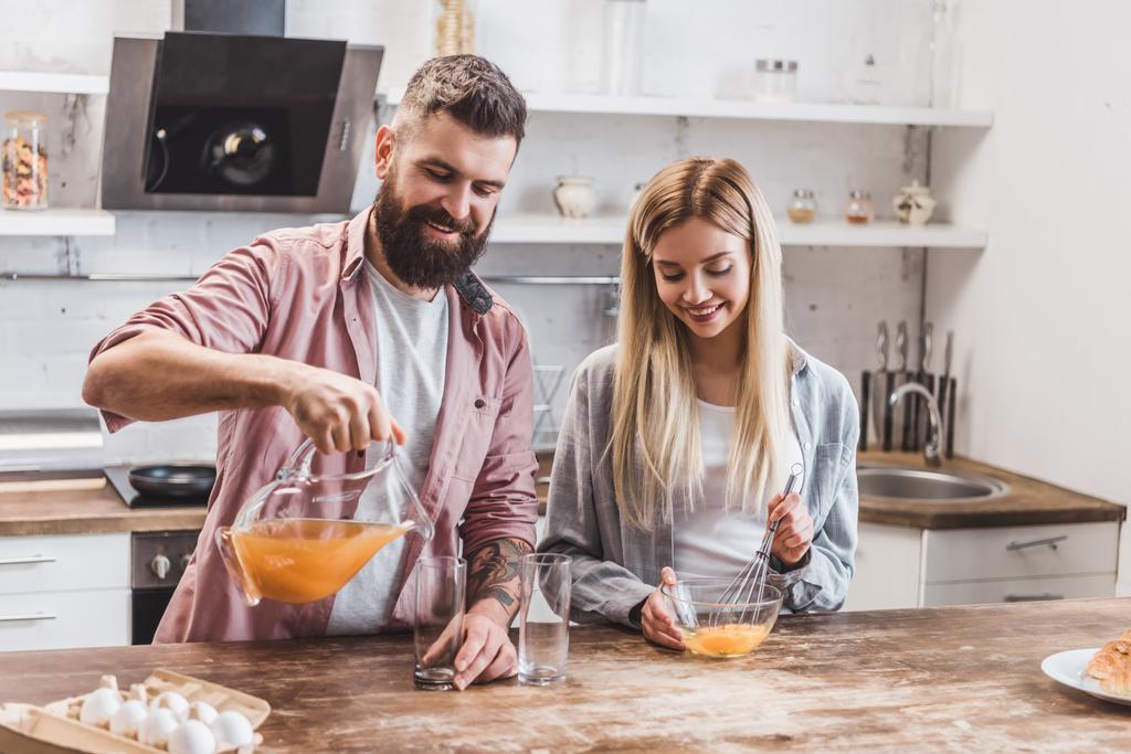 nuori pari valmistelee aamiaista yhdessä keittiössä ja juo mehua
 - Valokuva, kuva