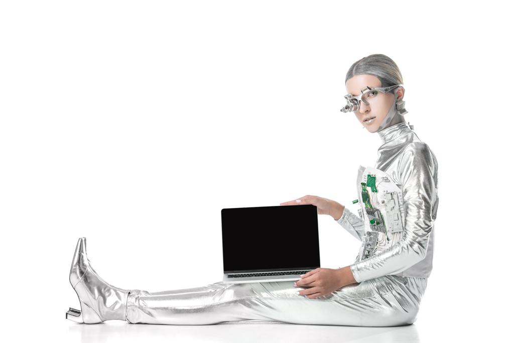 ασημένια ρομπότ κάθεται και δείχνει το laptop με κενή οθόνη που απομονώνονται σε λευκό, μελλοντική τεχνολογία έννοια - Φωτογραφία, εικόνα