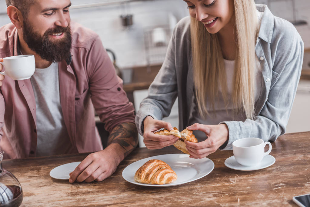 primo piano di coppia sorridente mangiare croissant e bere caffè al tavolo di legno
 - Foto, immagini