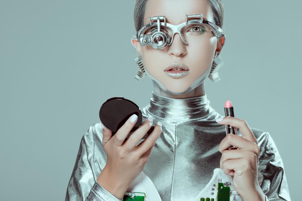 Silberroboter hält Spiegel und Lippenstift isoliert auf grauem, zukünftigem Technologiekonzept - Foto, Bild