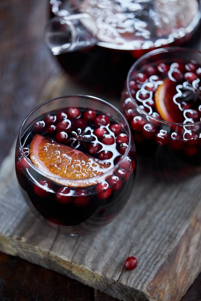 vista de alto ângulo de copos de vinho ruminado caseiro com cranberries e laranjas em suporte de madeira na cozinha
 - Foto, Imagem