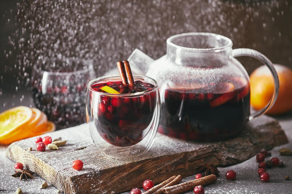 homemade mulled wine with cranberries in glasses and teapot with falling powdered sugar on table in kitchen - Photo, Image
