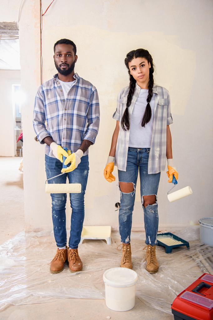 young couple with rolling brushes looking at camera during renovation of home - Photo, Image