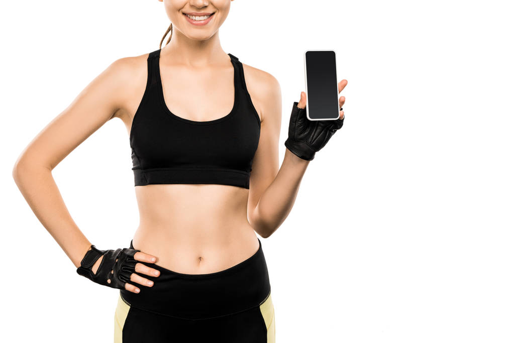 vista recortada de la deportista en forma de guantes de levantamiento de pesas que sostiene el teléfono inteligente con pantalla en blanco aislado en blanco
 - Foto, imagen