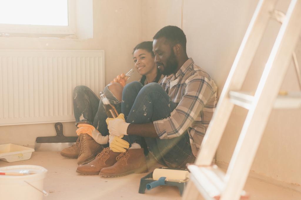 jonge Afrikaanse Amerikaanse echtpaar bier drinken op vloer terwijl het maken van de renovatie van woning - Foto, afbeelding